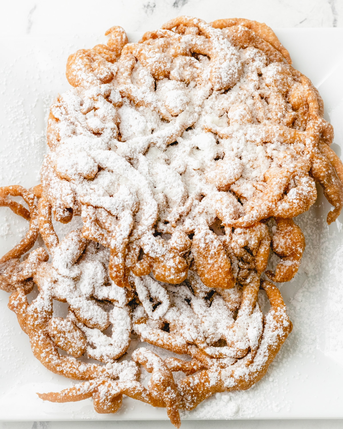 Two funnel cakes shingled on top of each other and covered in powdered sugar.