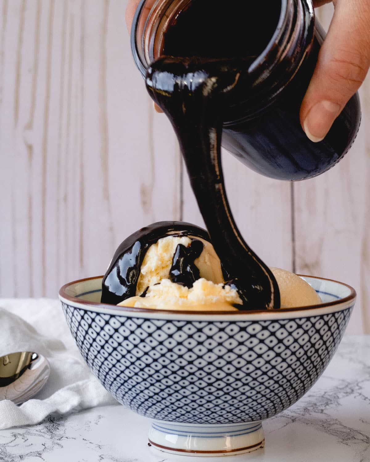 Pouring hot fudge from a mason jar onto a bowl of ice cream.