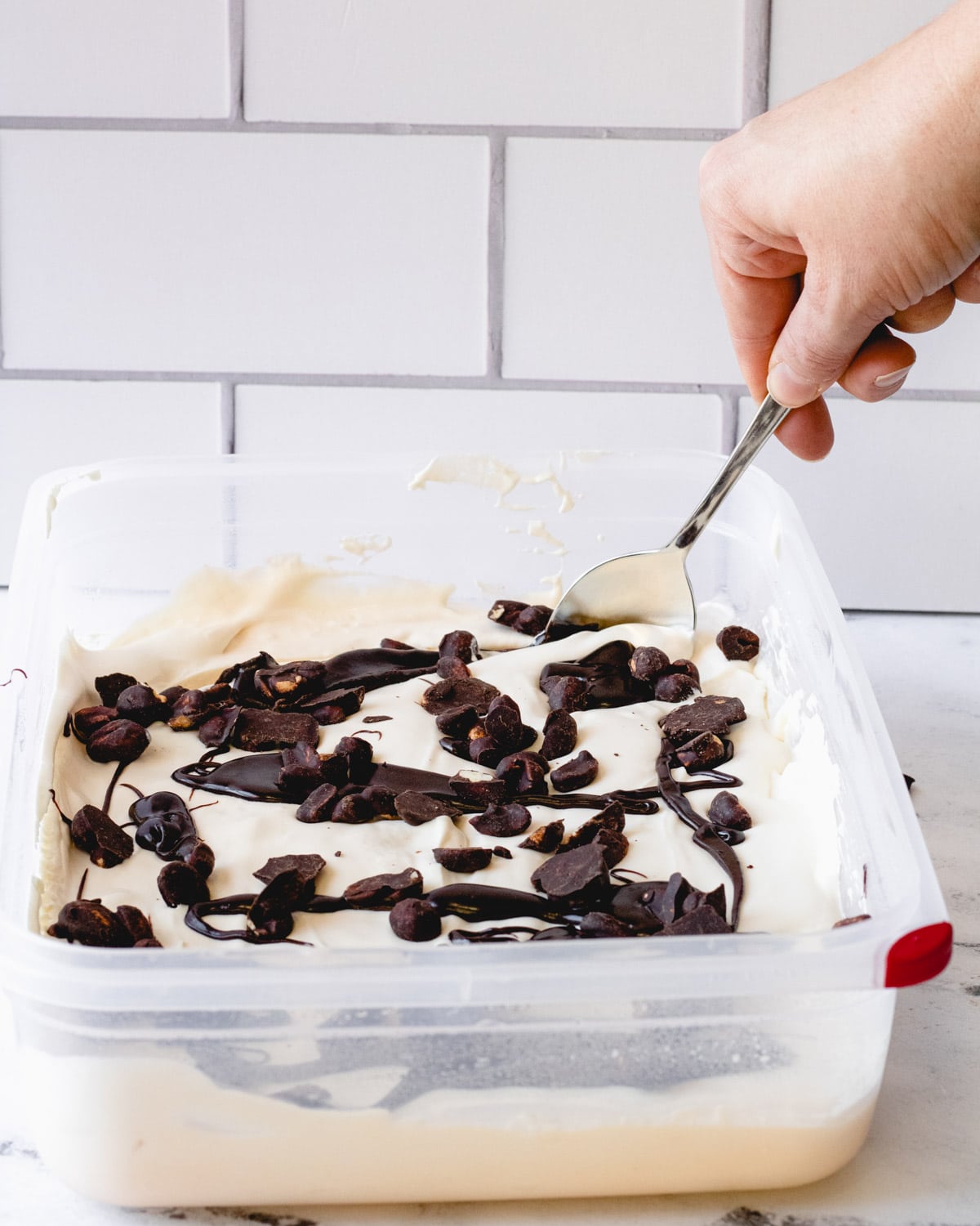 Using spoon to swirl fudge ripples and peanuts into ice cream.