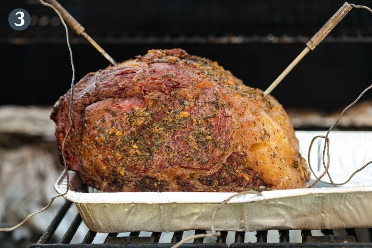 Herb crusted rib roast in smoker with thermometer probes inserted.