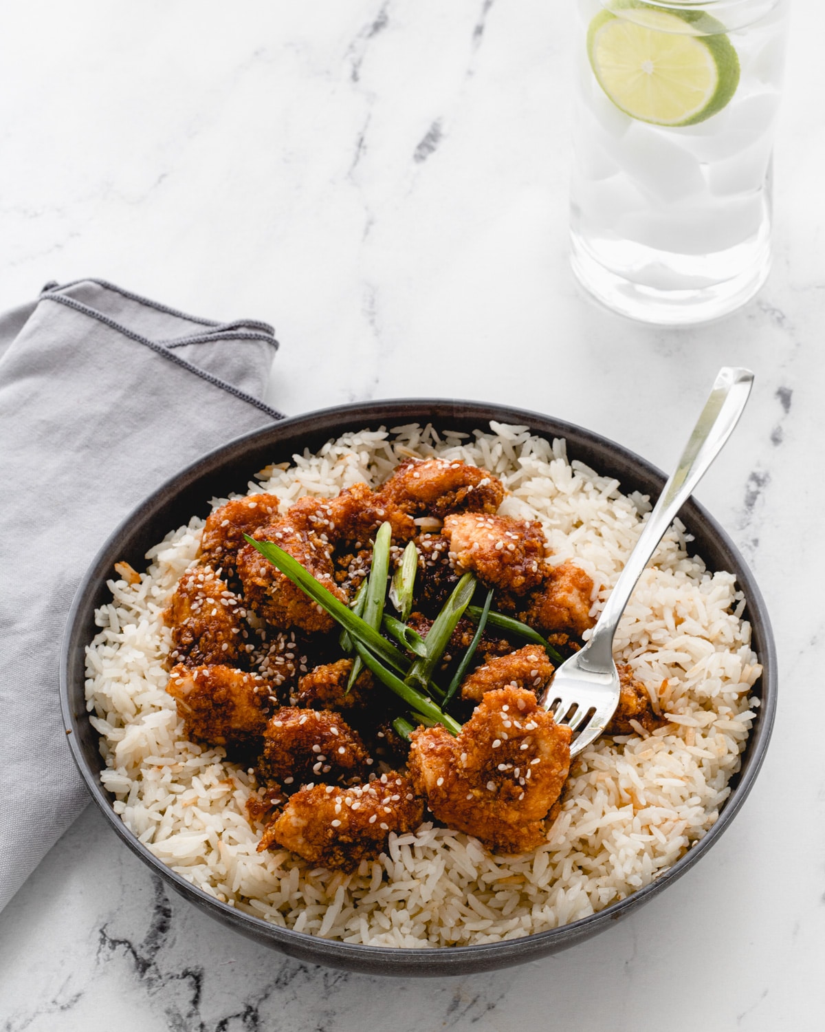 Bowl of sticky garlic chicken bites on rice, topped with green onions.