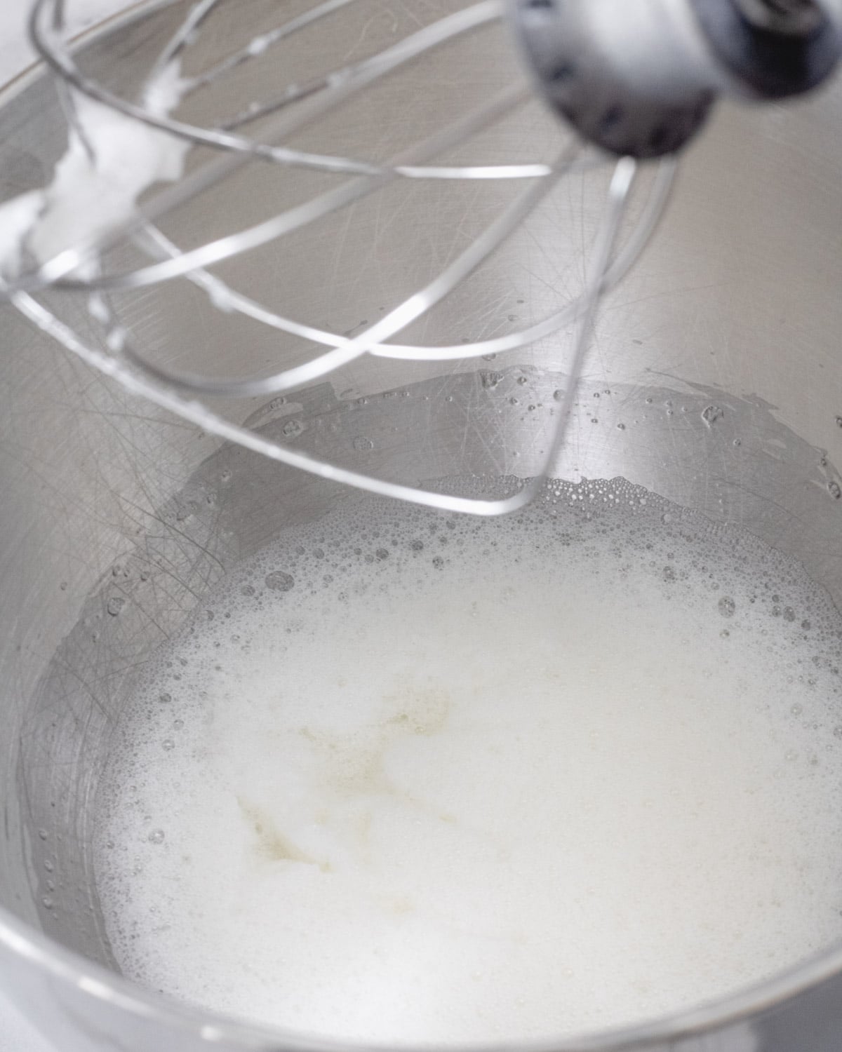 Large bowl with frothy egg whites, and whisk beater at the top.