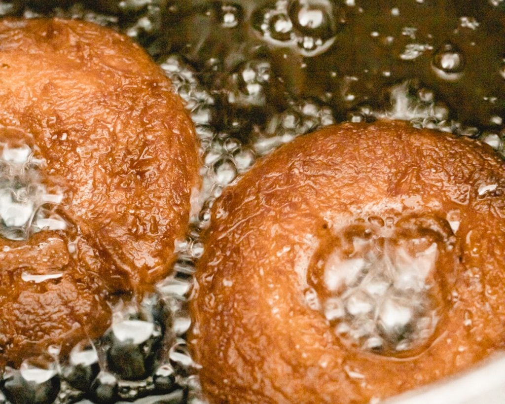 Two donuts being fried in hot oil.
