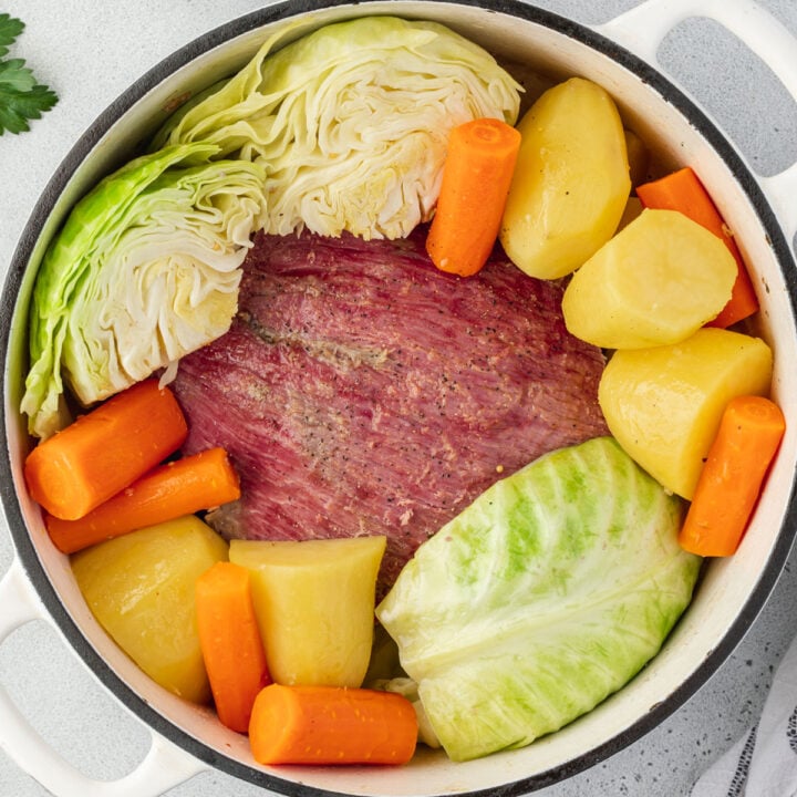 Cooked corn beef in a Dutch oven surrounded by potatoes, carrots, and cabbage.