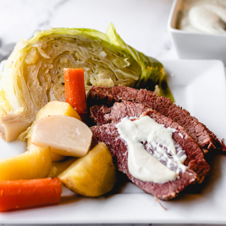 Corned beef on a plate with boiled vegetables and mustard sauce smeared across the beef.