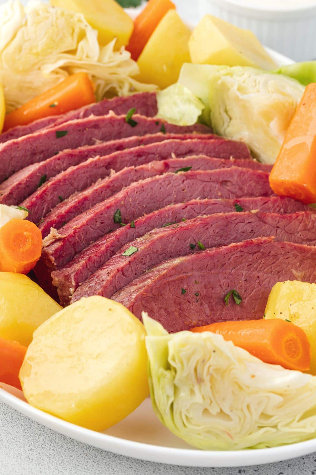 Bright pink slices of corned beef on a platter with yellow potatoes, cooked carrots, and cabbage wedges.