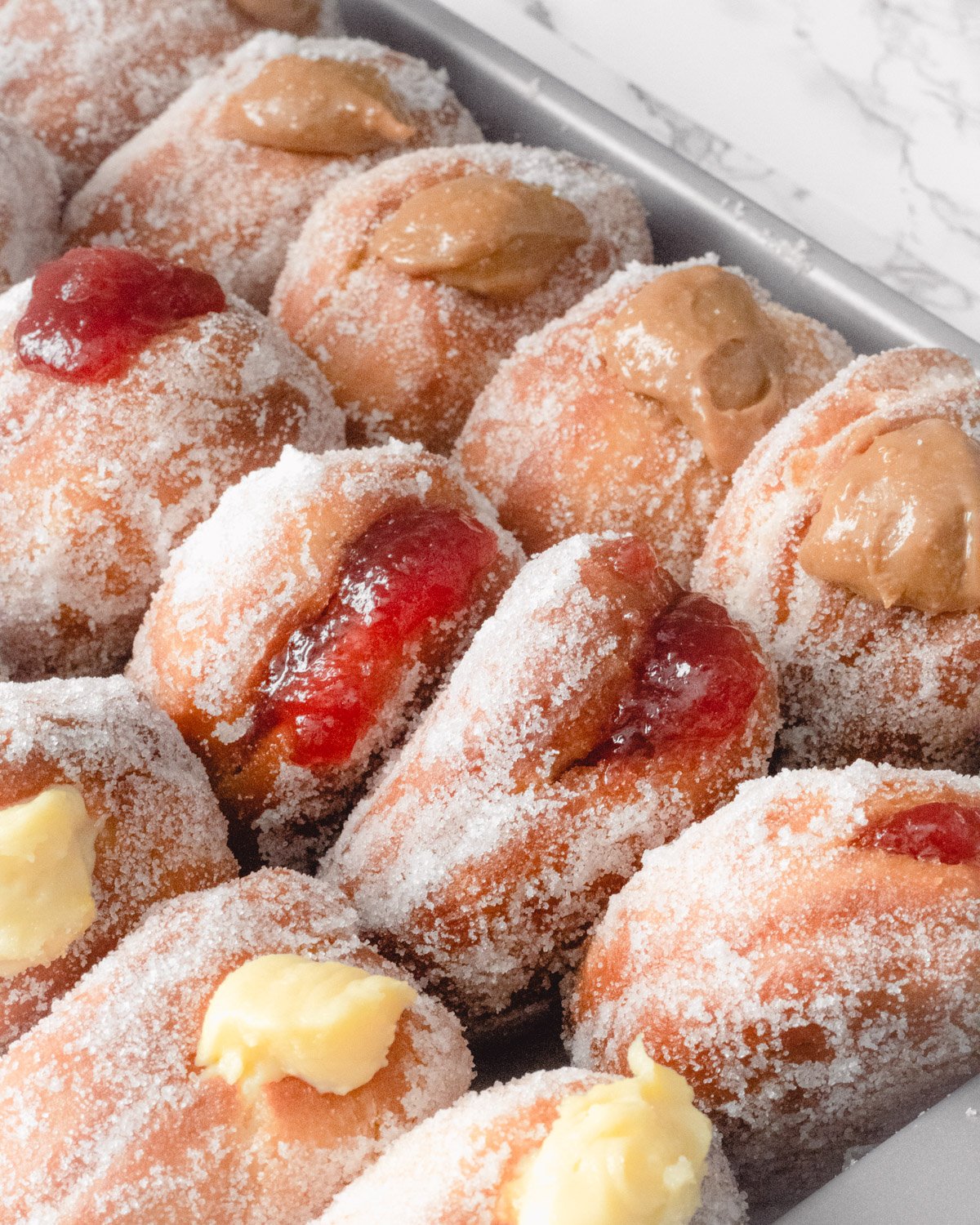 A tray of sugar coated paczki Polish donuts with different fillings.