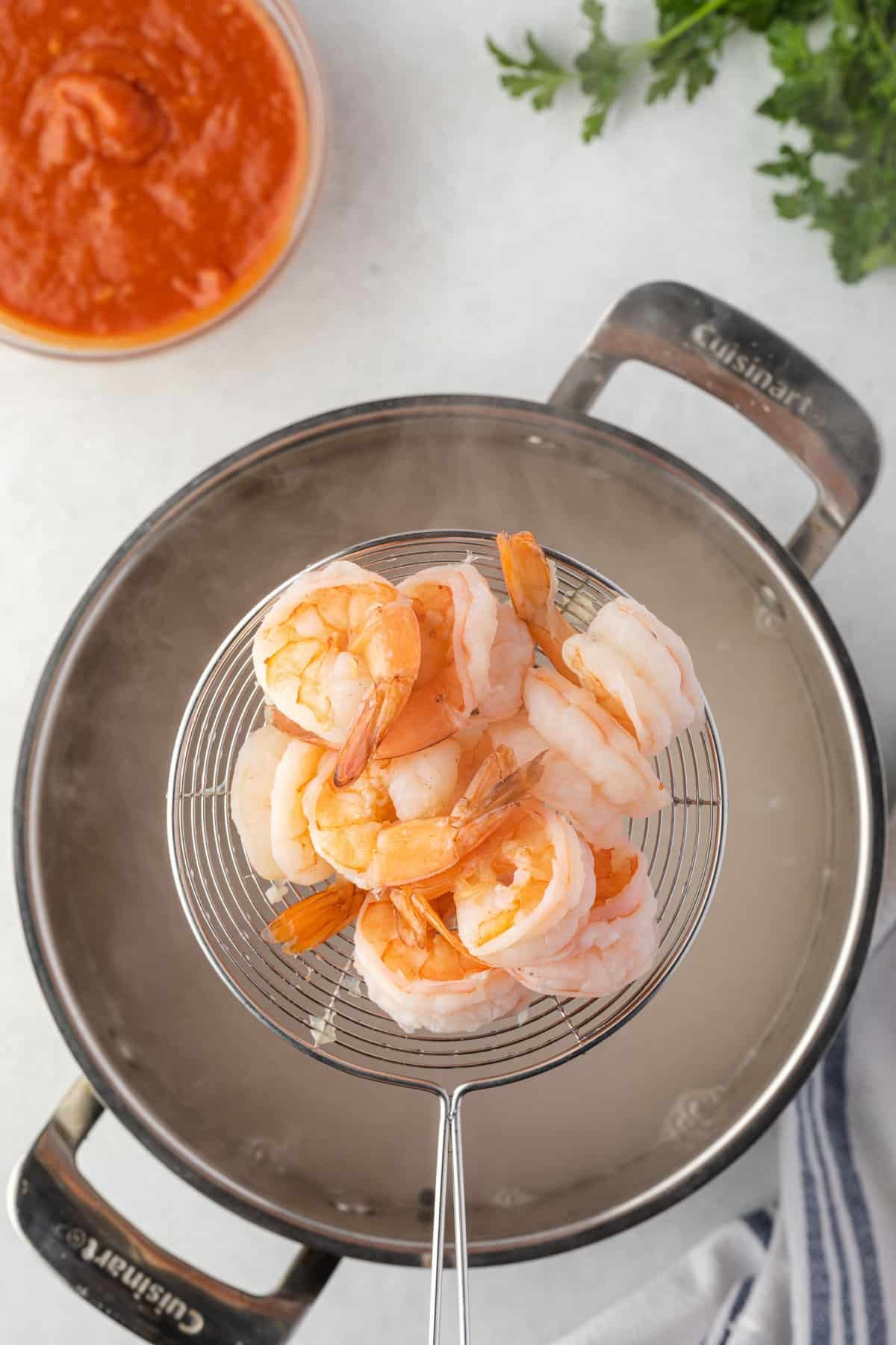 A wire slotted spoon pf cooked shrimp held over a steaming pot.