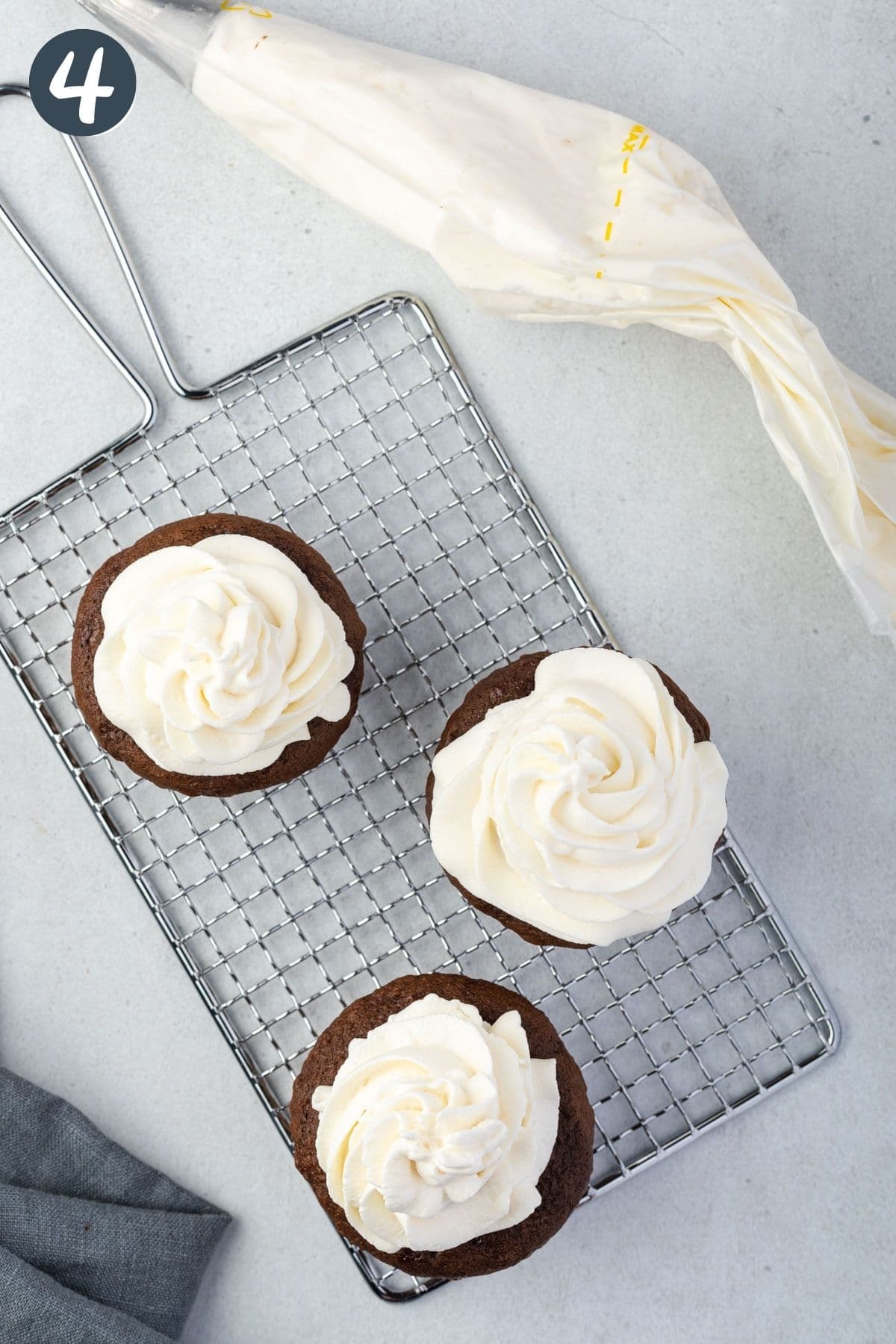 3 cupcakes on a cooling rack topped with stabilized whipped cream.