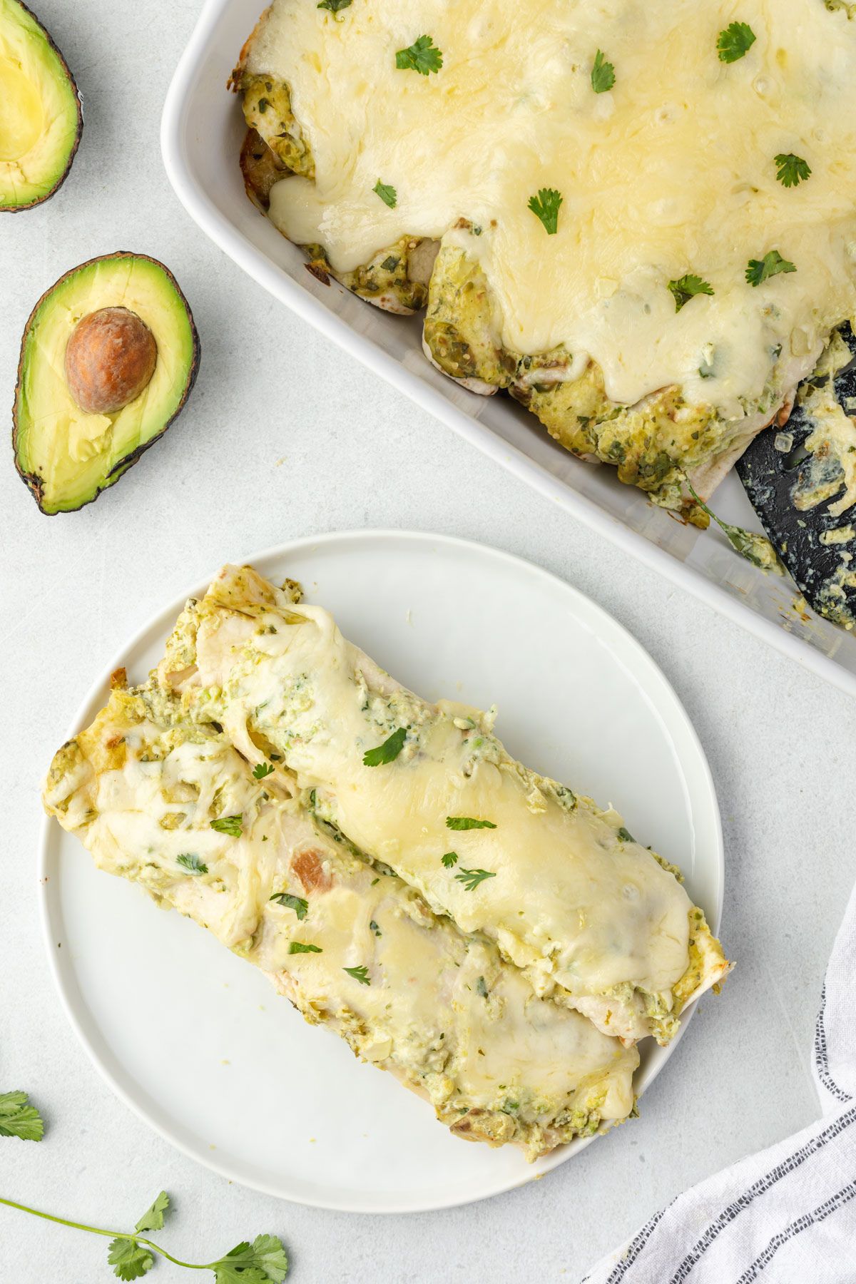 Two green chile enchiladas on a plate with pan in the top corner.