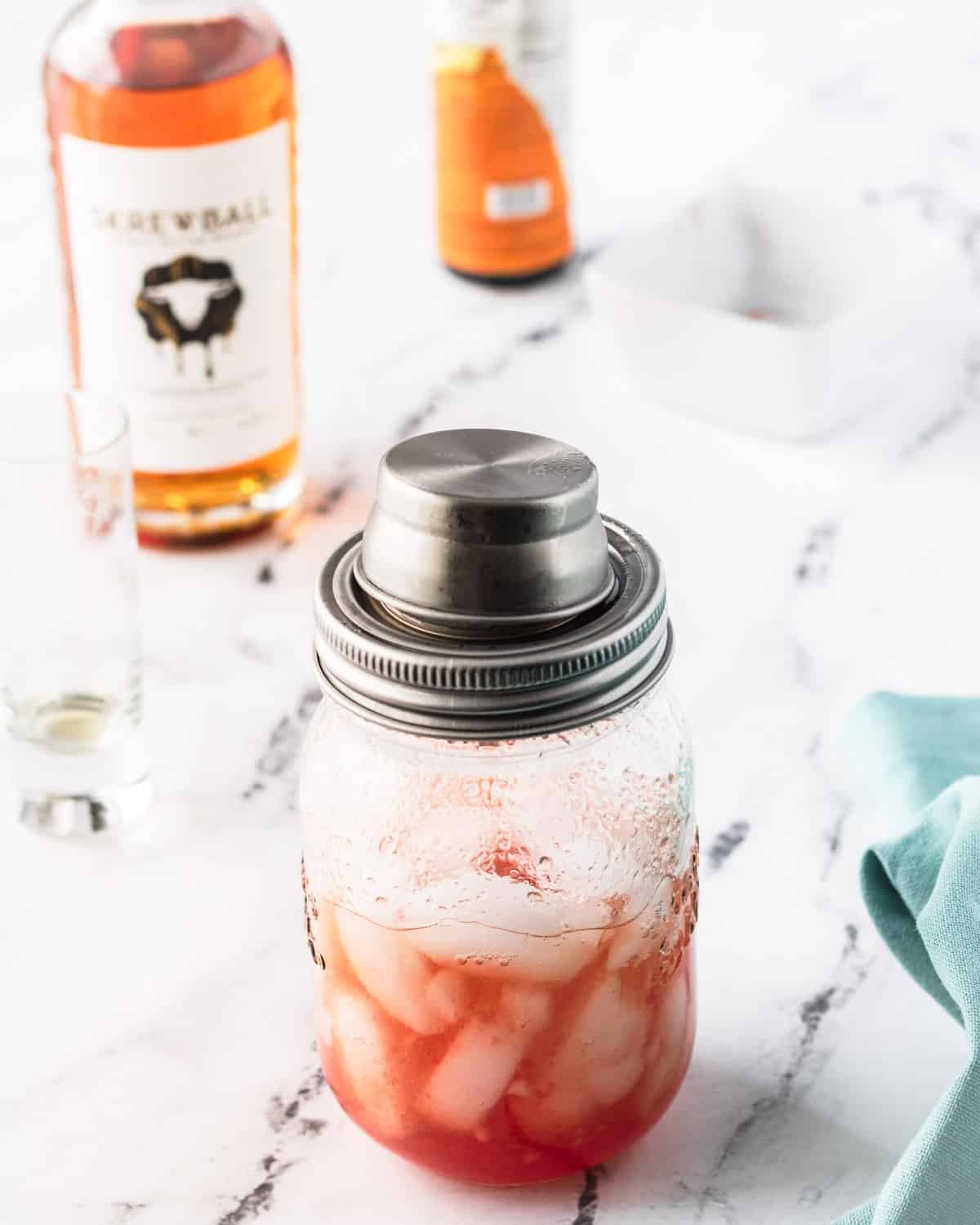 Mason jar with shaker lid on it, and the cocktail ingredients shaken together.