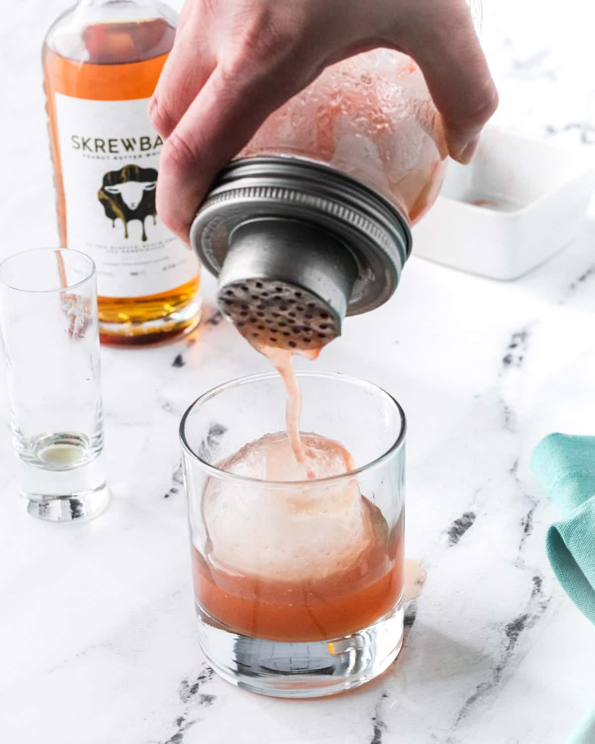 Pouring the cocktail into a rocks glass with a round ball ice cube.