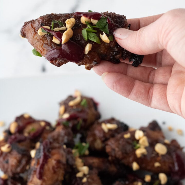 Holding a PB&J wing garnished with peanuts, cilantro, and blackberry coulis, over a plate of wings.