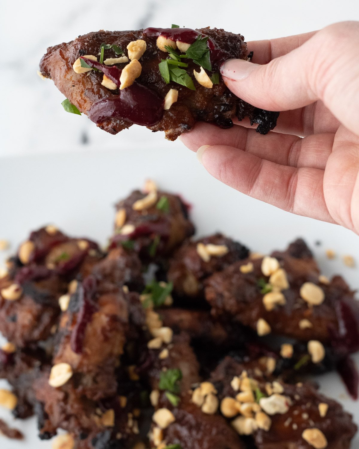 Holding a PB&J wing garnished with peanuts, cilantro, and blackberry coulis, over a plate of wings.