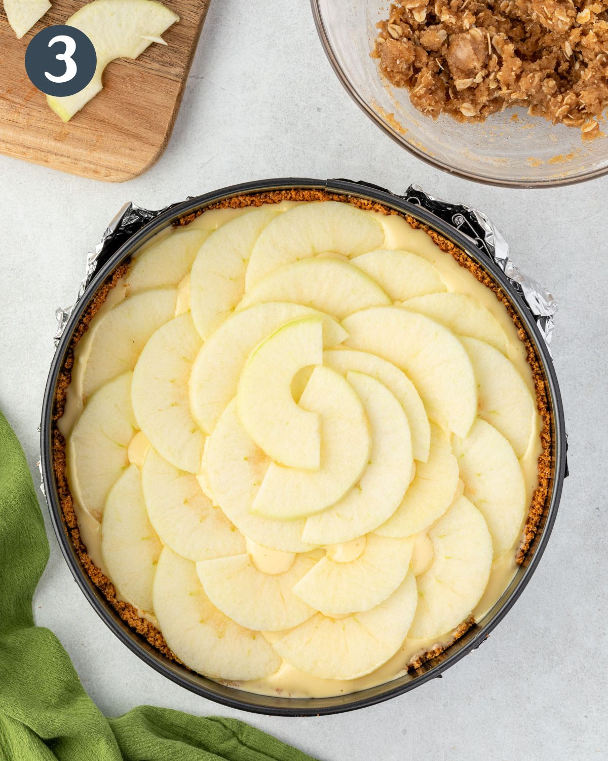 Apple slices are arranged in a circular pattern on top of the cheesecake batter.