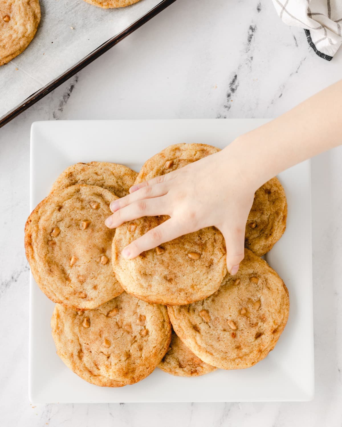 A small child reaching in to grab a cookie off of the plate.