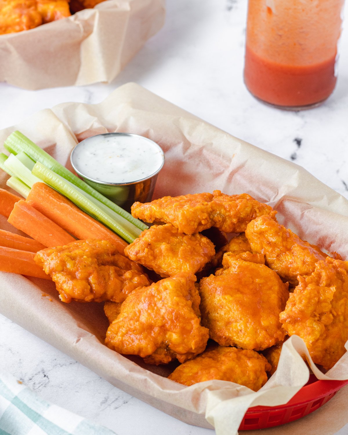 Basket of air fryer boneless chicken wings with ranch dip, carrots, and celery.