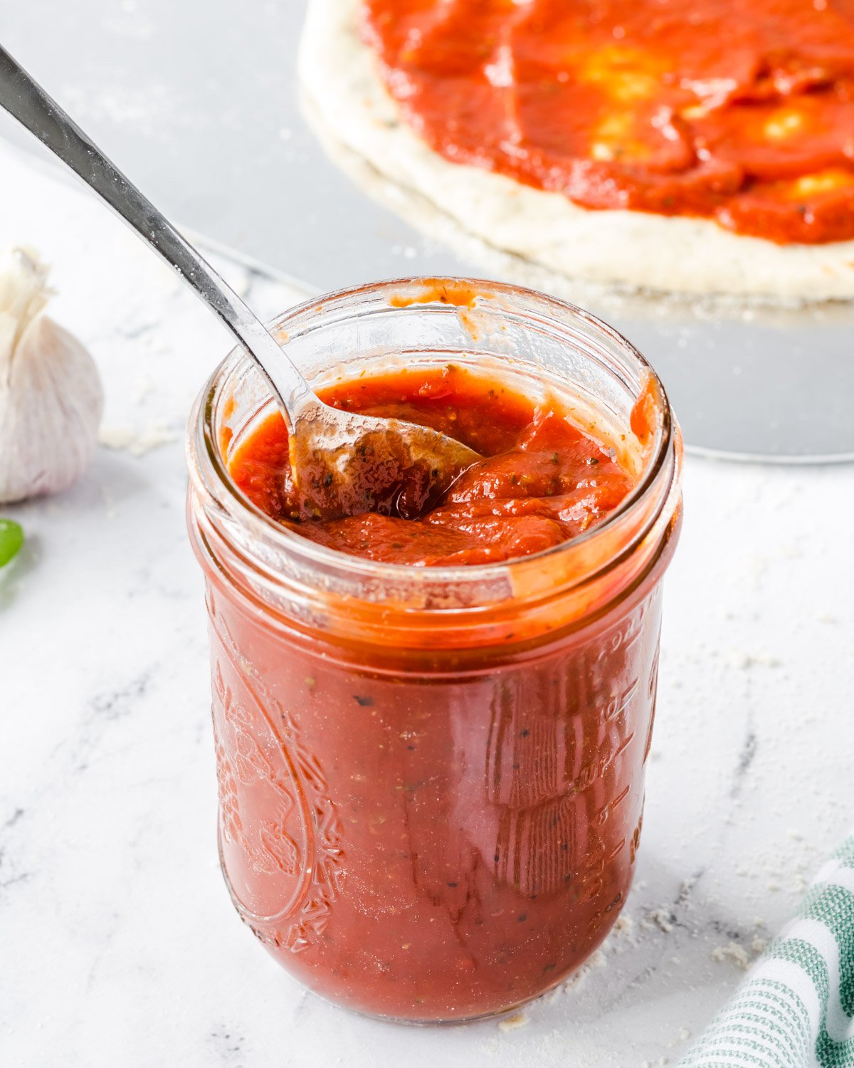 Mason jar of pizza sauce with a topped pizza in background.