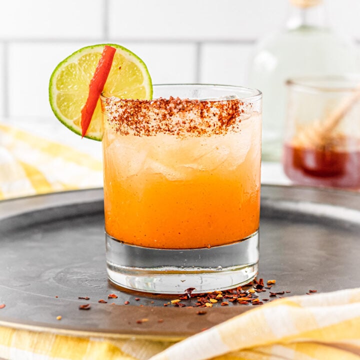 Rocks glass with hot honey margarita, chili-salt rim and a lime and hot pepper wedge.