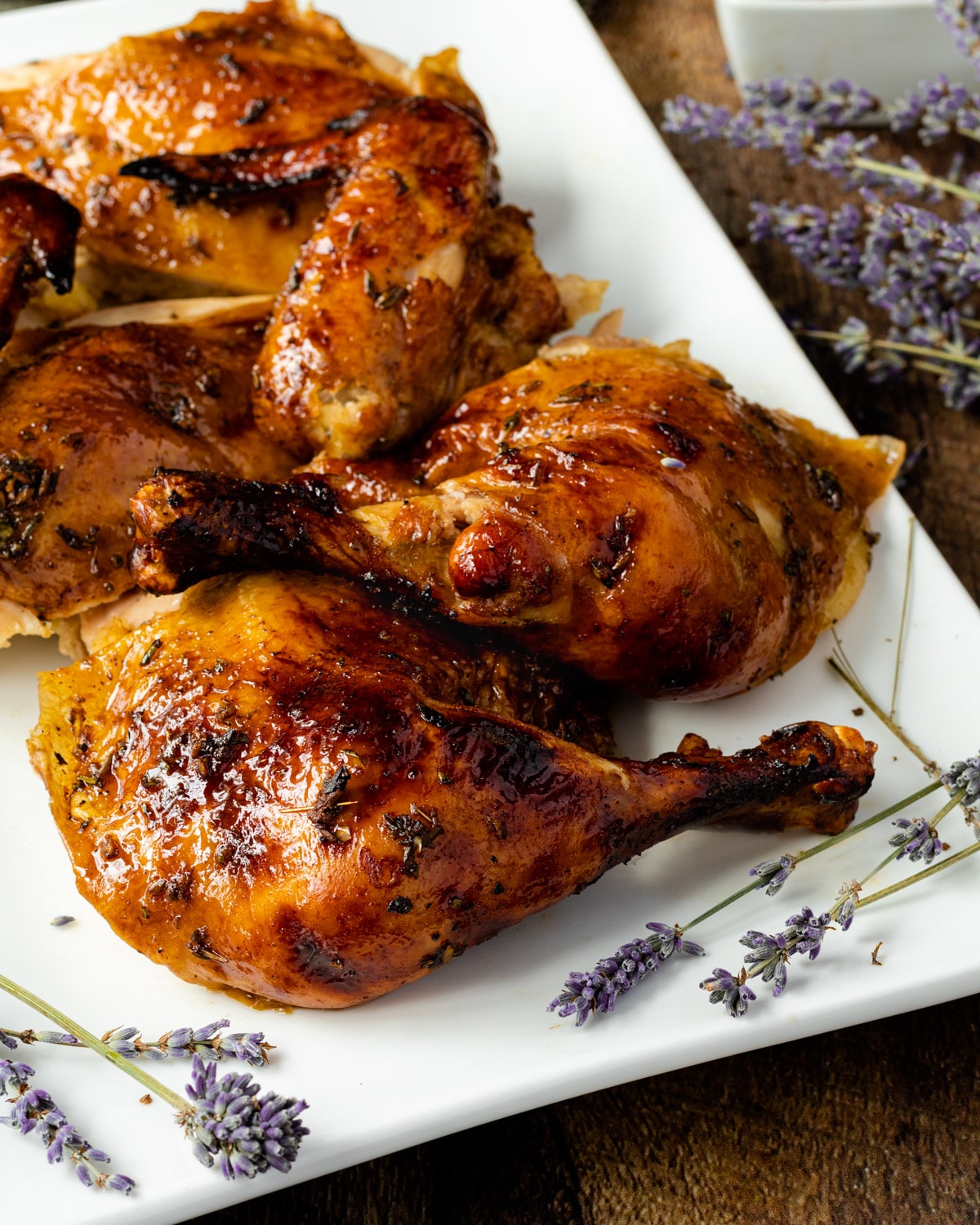 Chicken pieces roasted with lavender and herbs, on a white rectangular plate, with lavender sprigs across it.