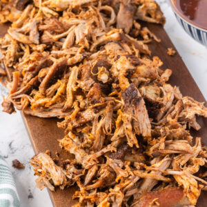 Pulled pork on a wooden board, with bowl of bbq sauce.