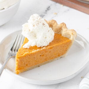 Slice of sweet potato pie on a round plate with a dollop of whipped cream on top.