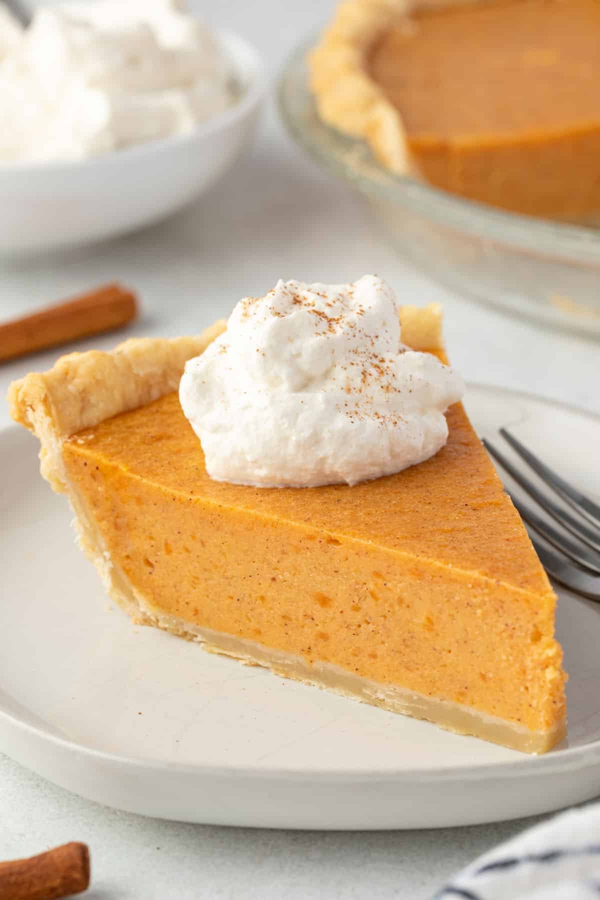 Slice of sweet potato pie on a round plate with a dollop of whipped cream on top.