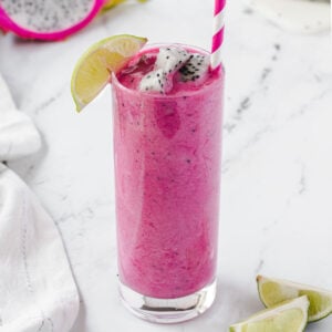 Bright pink dragon fruit smoothie, with white dragonfruit chunks and a lime wedge as garnish.