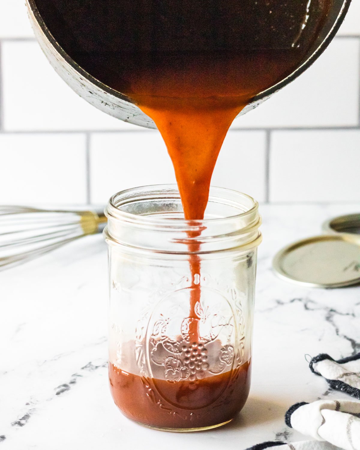 Pouring sauce from the pan into a mason jar.