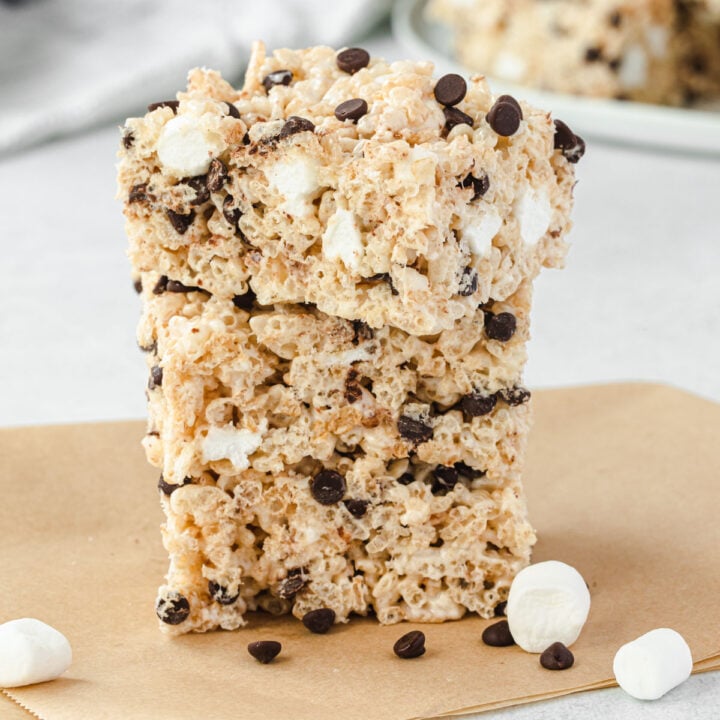Stack of 3 chocolate chip rice krispie treats with some mini marshmallows and chips sprinkled on parchment.