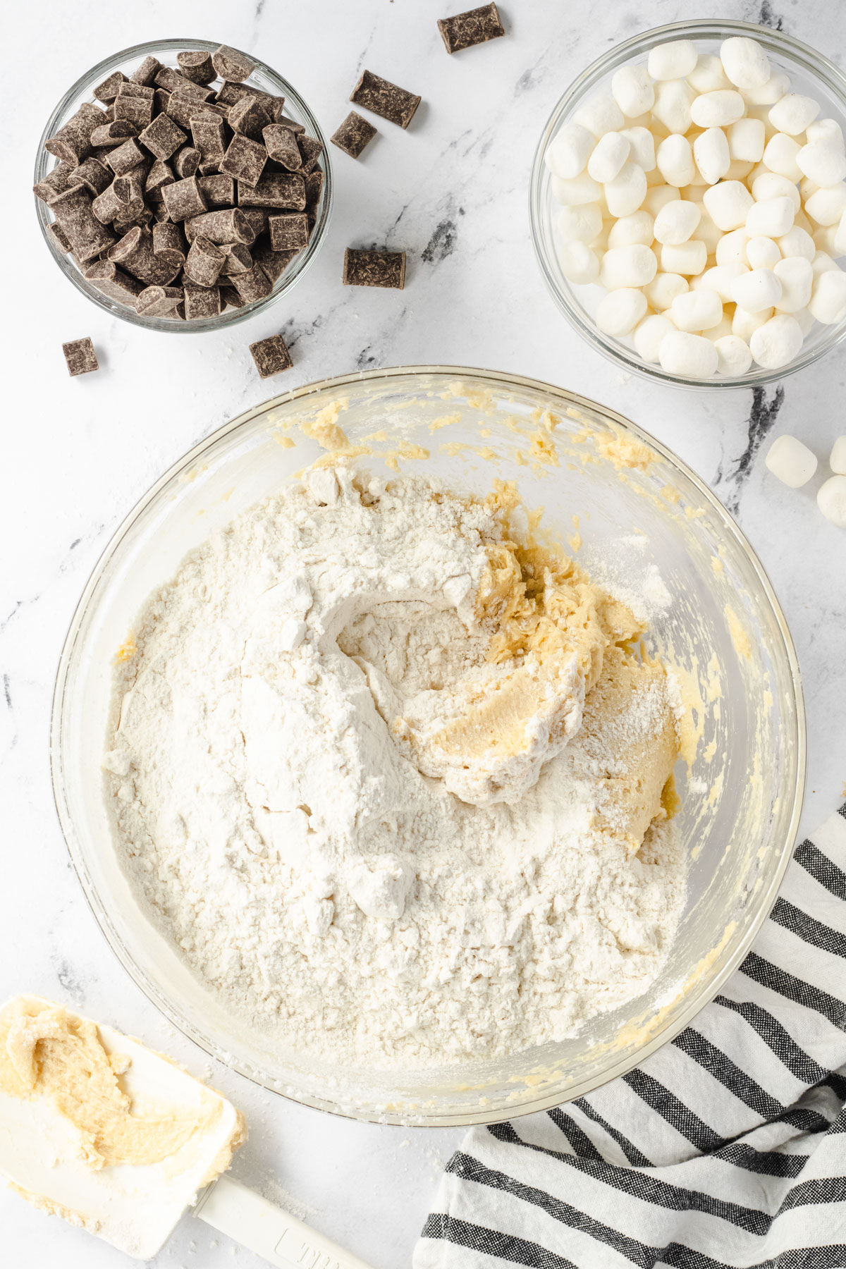 Flour added to the cookie dough bowl, bowls of chocolate chips and marshmallows at the top of the photo.