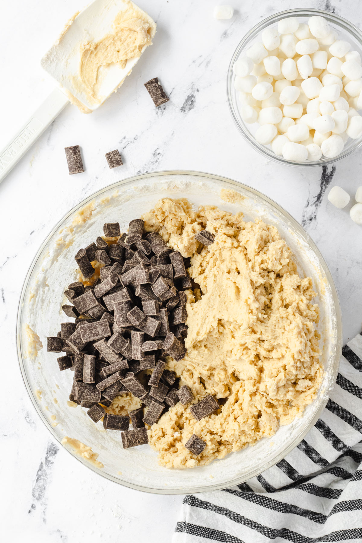 Cookie dough with chocolate chips added, and a bowl of marshmallows next to it.