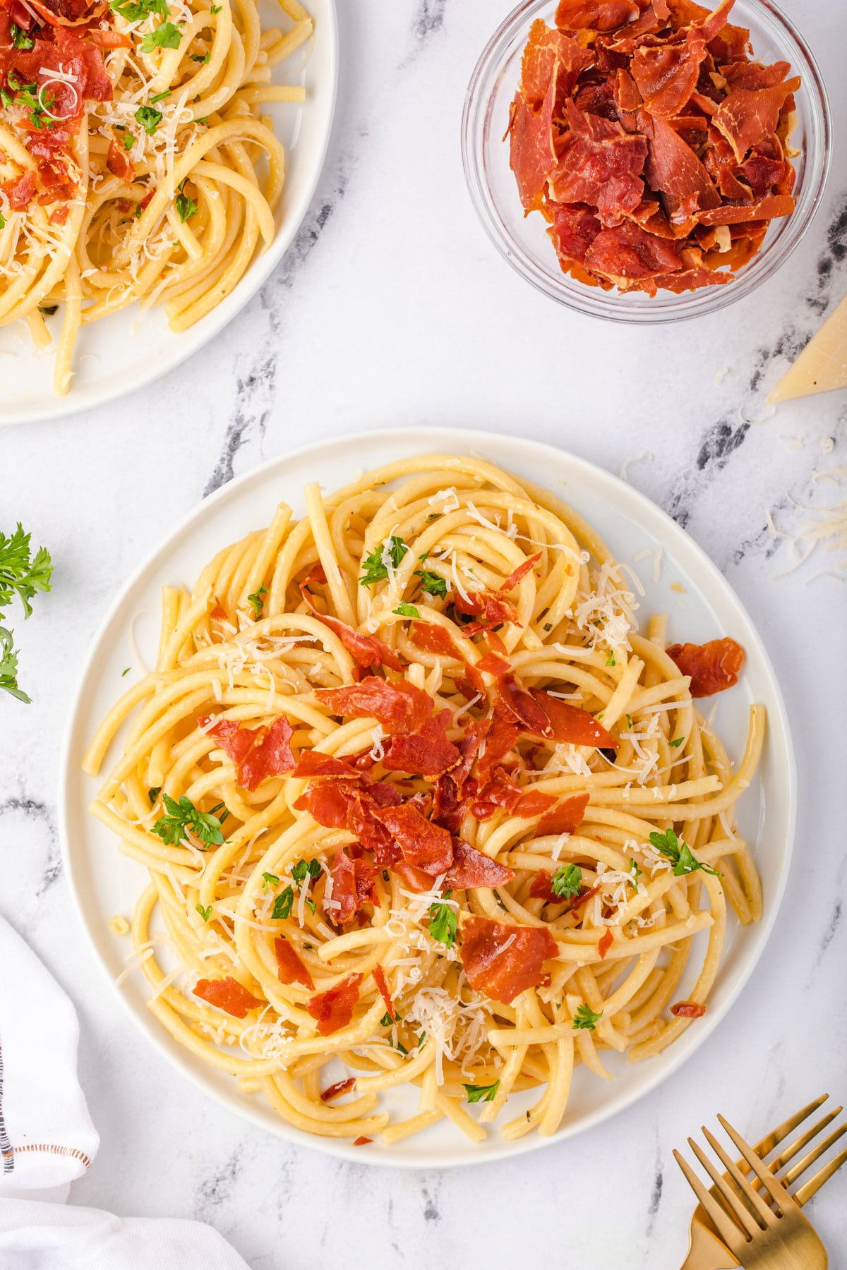 Two plates of pasta and a bowl of crispy prosciutto.