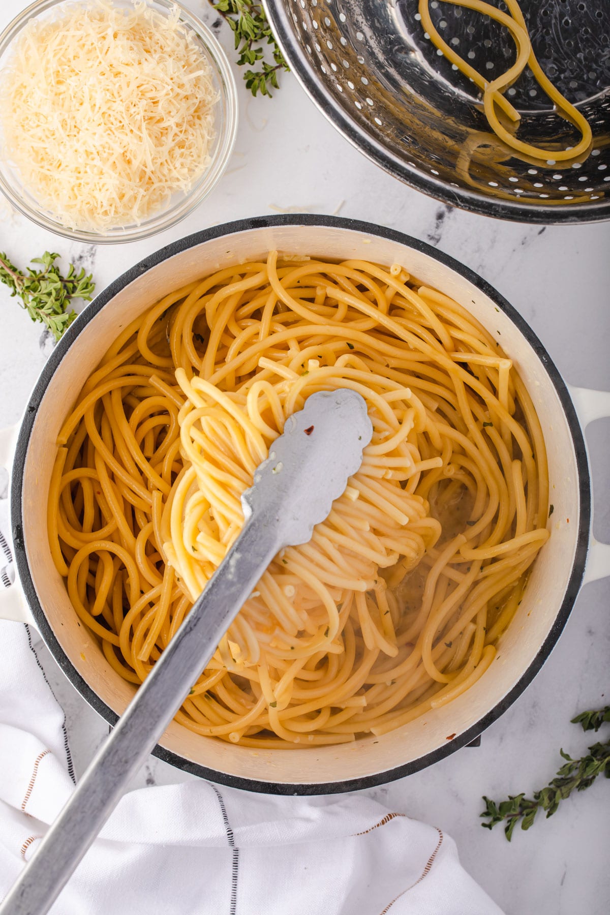 Tossing pasta with tongs to mix into sauce.