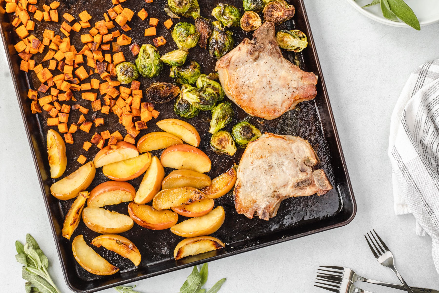 Sheet pan angled with roasted dinner on it, and sage leaves framing the pan.