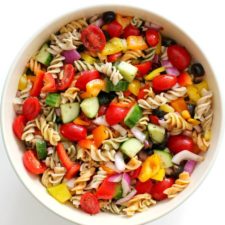 Bowl of pasta salad with tomatoes, cucumber, olivers, and peppers.