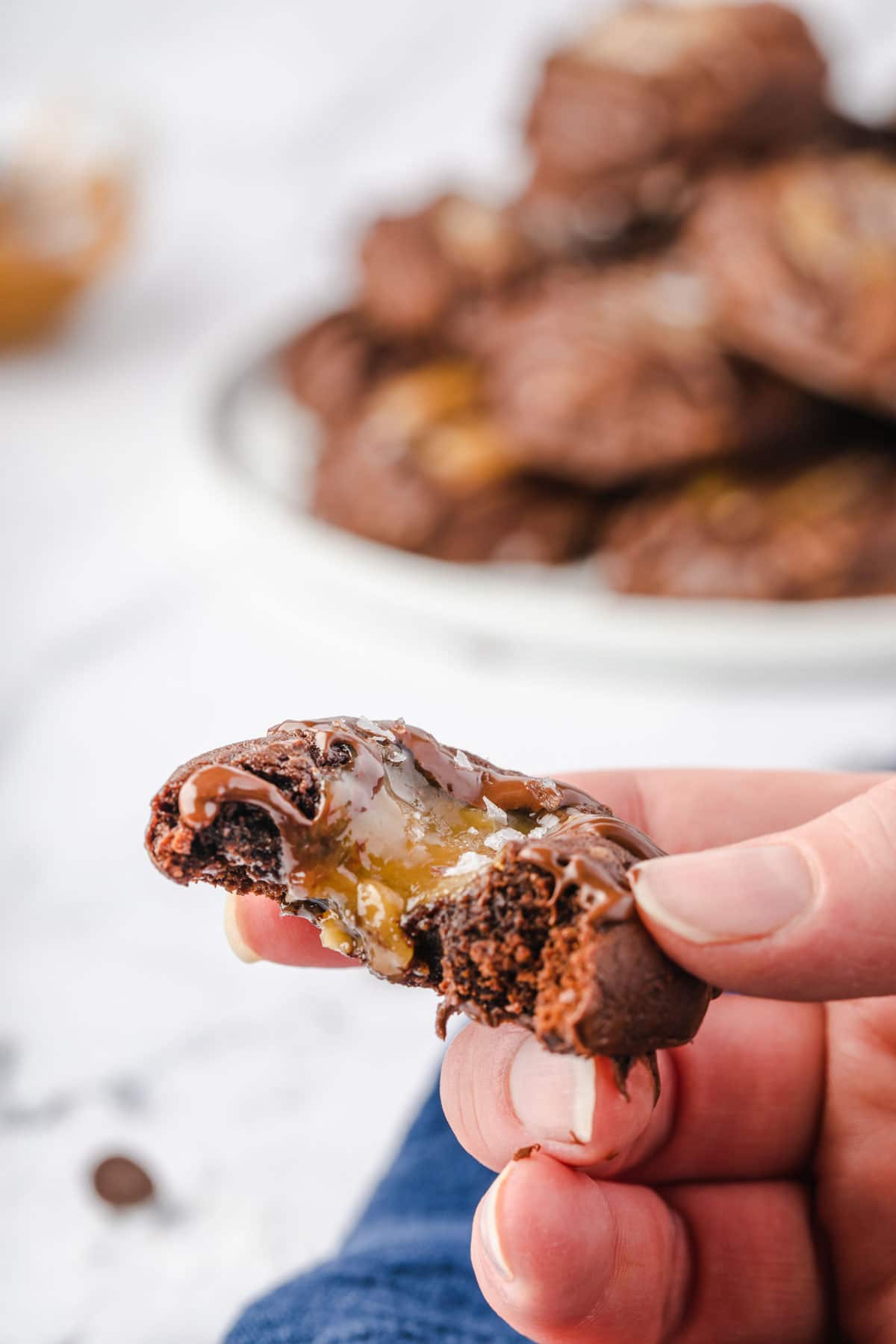 Hand holding caramel brownie cookie with a bite out of it and caramel starting to drip.