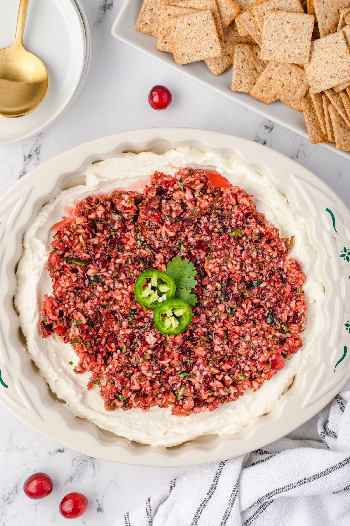 Finished cranberry jalapeno cream cheese dip in center with plate of crackers in corner.