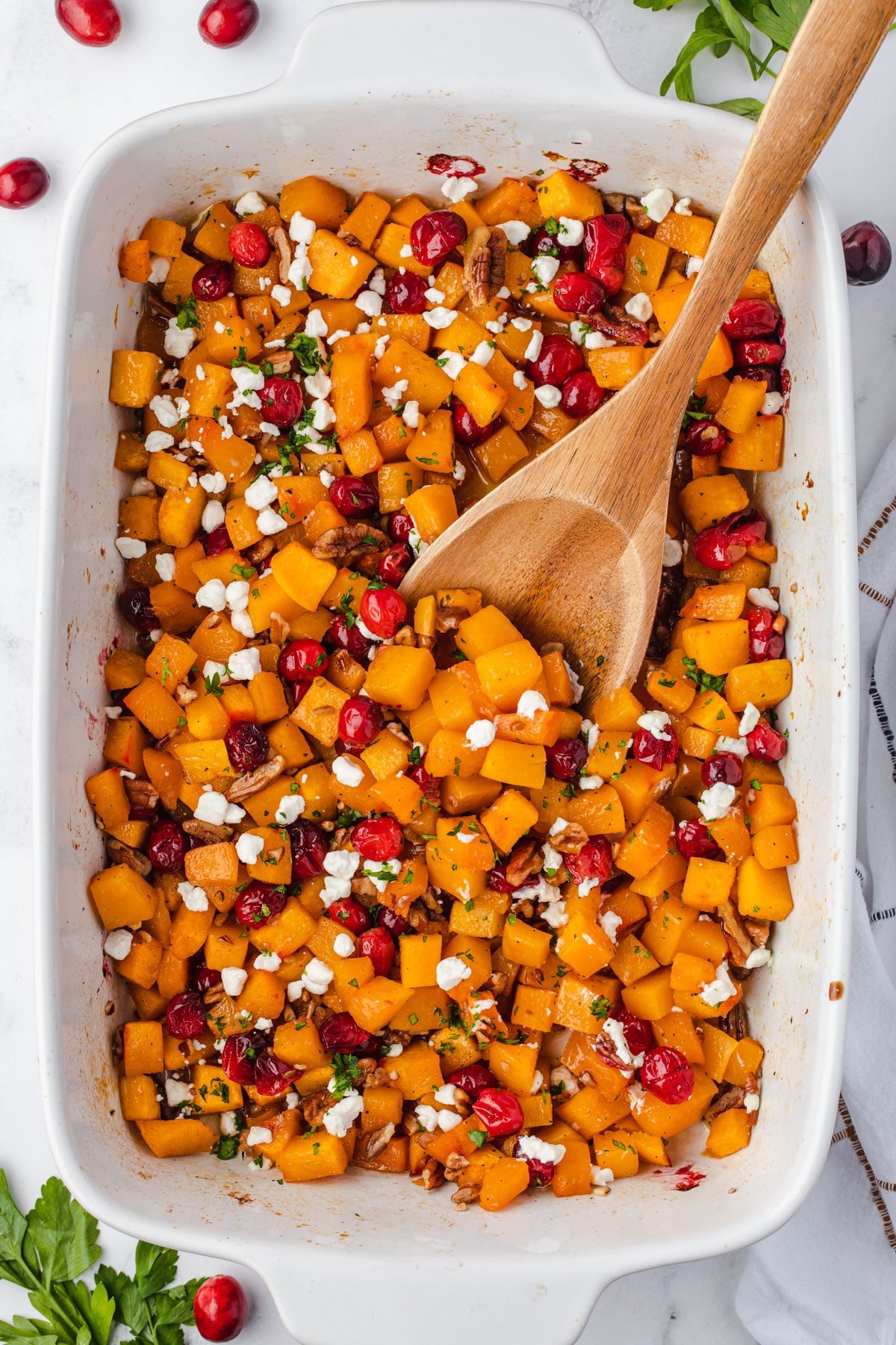 9x13 pan with a wooden spoon scooping out some butternut squash with cranberries, pecans, and goat cheese.