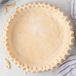 Unbaked pie crust in a pie plate with edges crimped and pieces of dough scattered around.