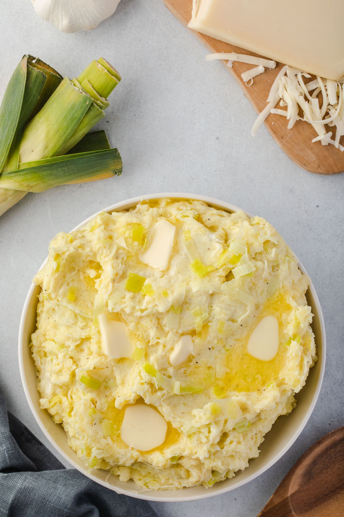 Scooping out some mashed potatoes with a wooden spoon, leek, garlic, and gruyere in background.