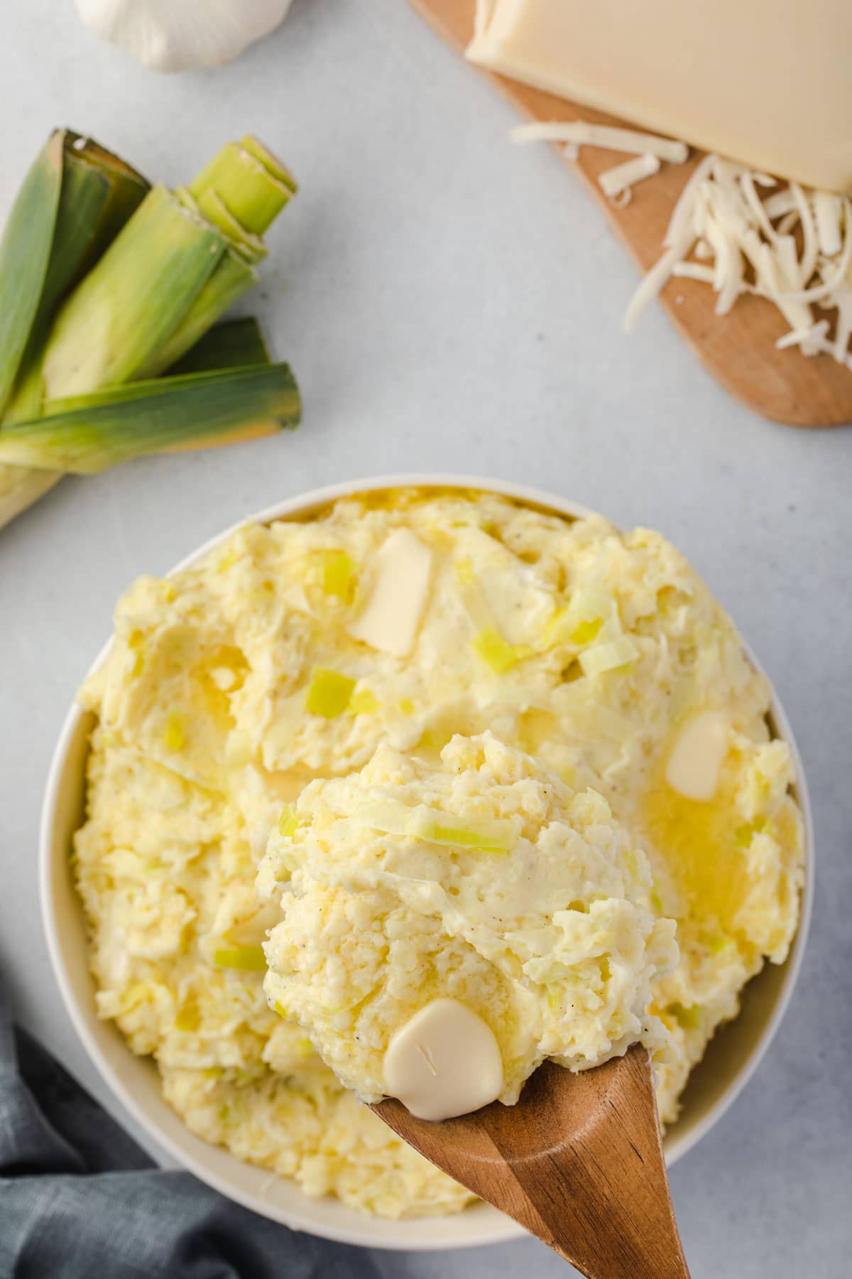 Overhead of mashed potatoes with pools of butter, scooping some out with a wooden spoon.