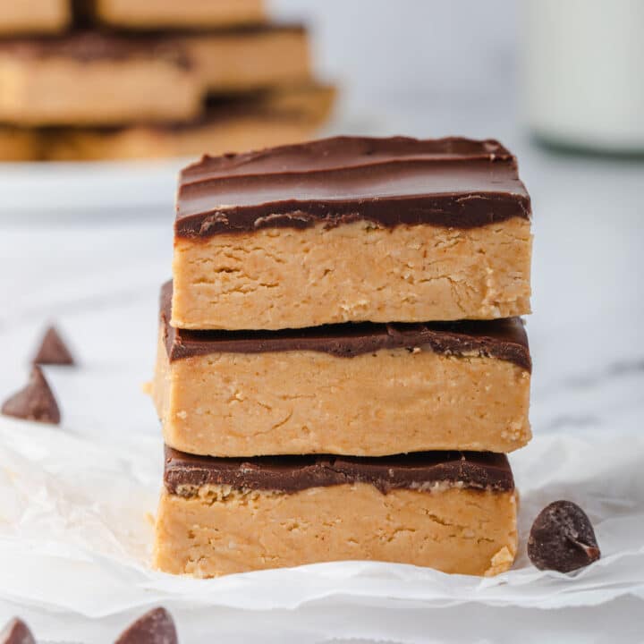 Stack of 3 no bake peanut butter buckeye bars with a plate of bars in background.