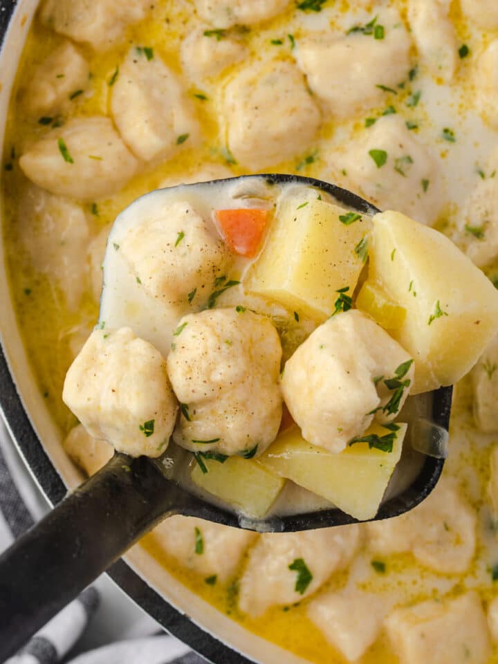 Scooping out knoephla soup from Dutch oven with a black ladle.