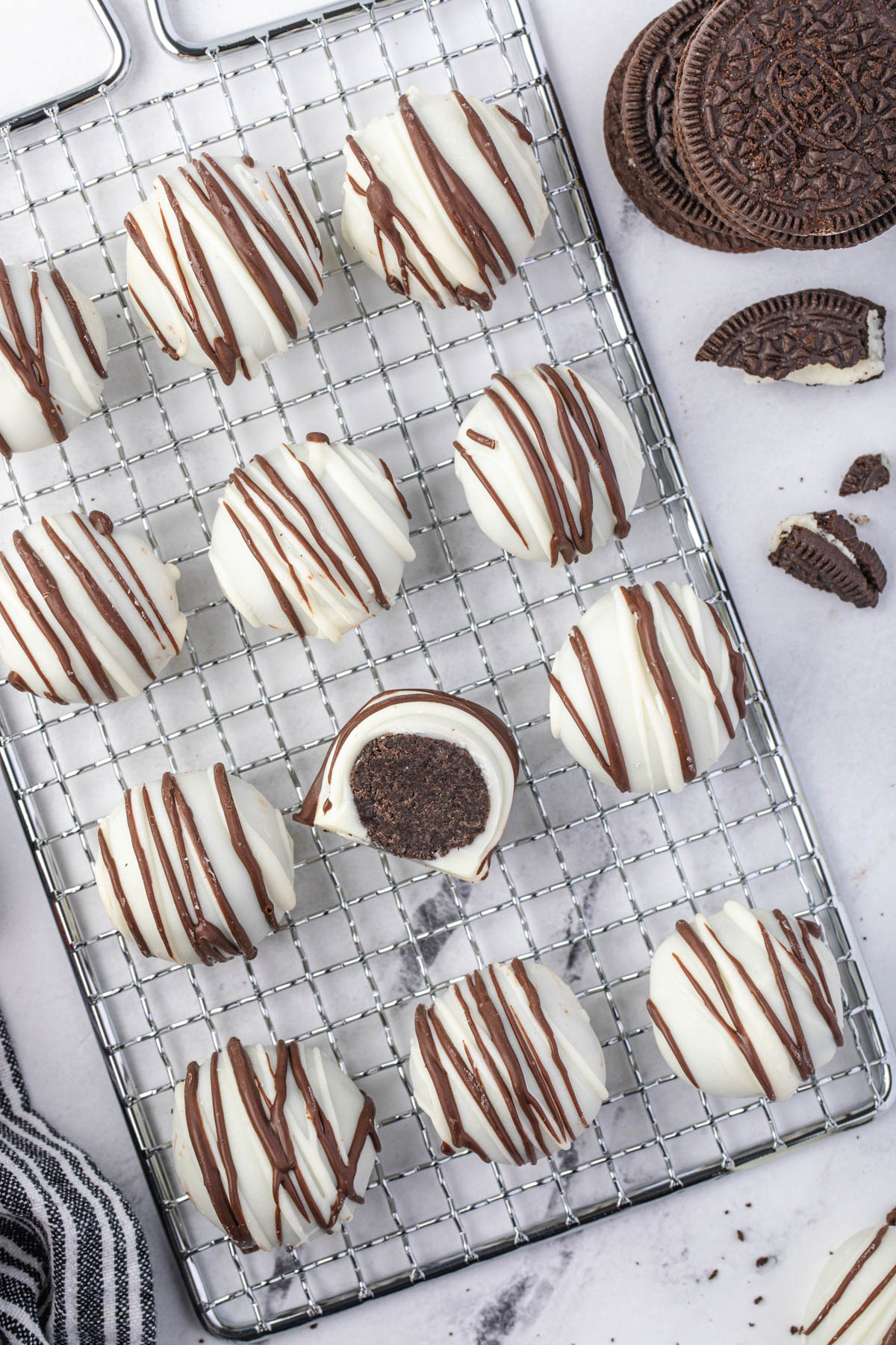 Oreo balls on a cooling rack after being drizzled with chocolate.