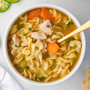 Overhead of a bowl of soup with egg noodles, chunks of chicken, and carrot slices.