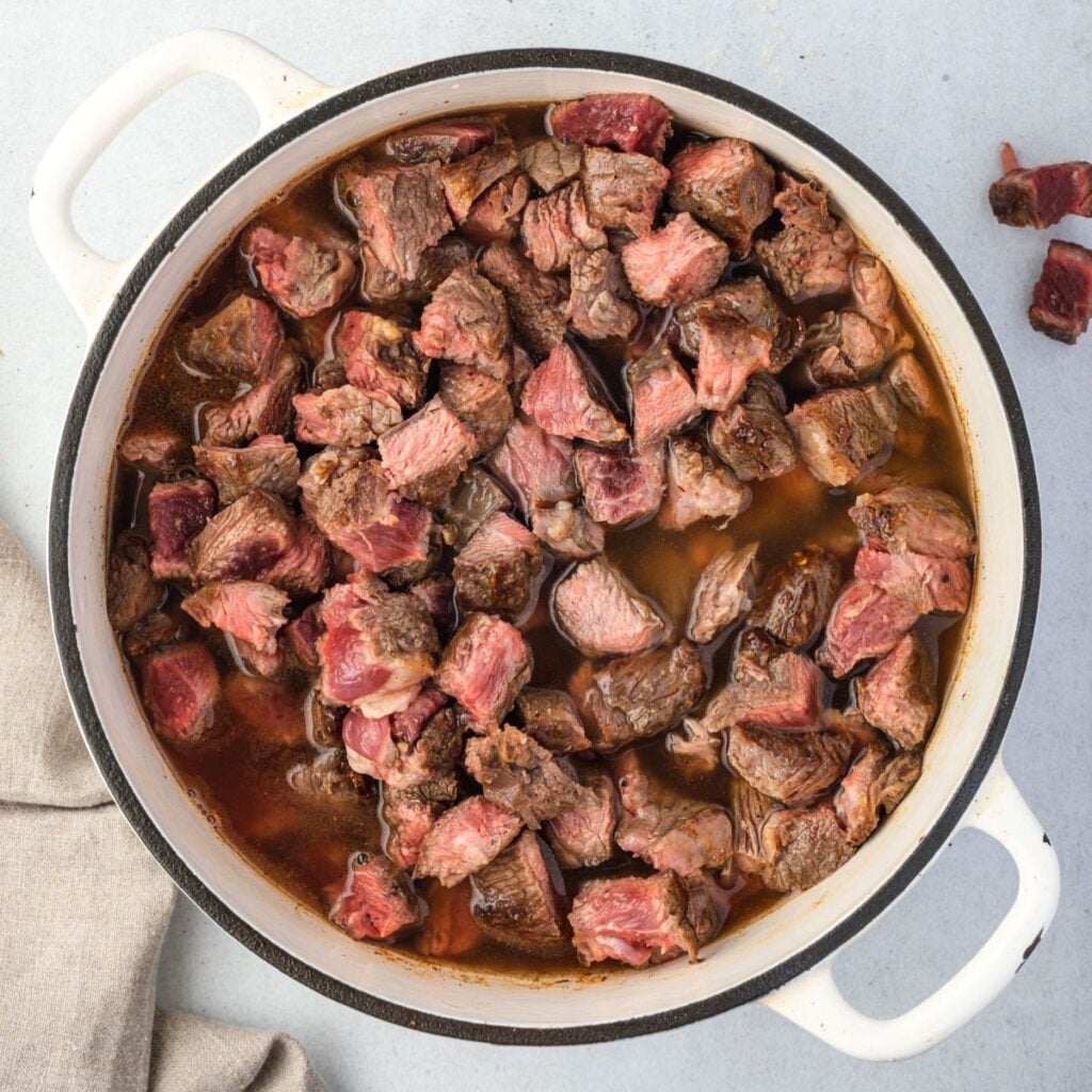 Bite sized pieces of beef with searing on the outside, rare in the center, in red liquid.