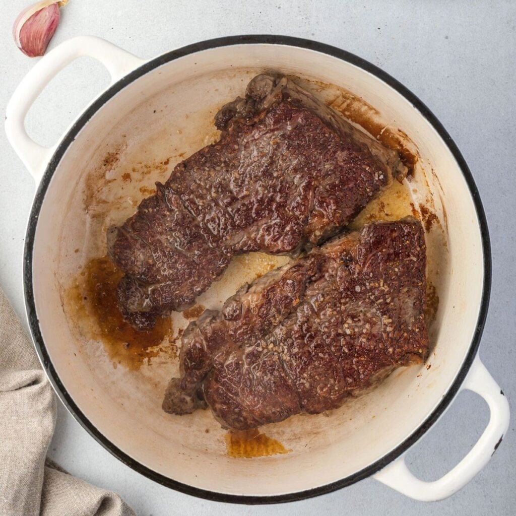 2 slabs of chuck roast seared dark and glistening in a dutch oven.