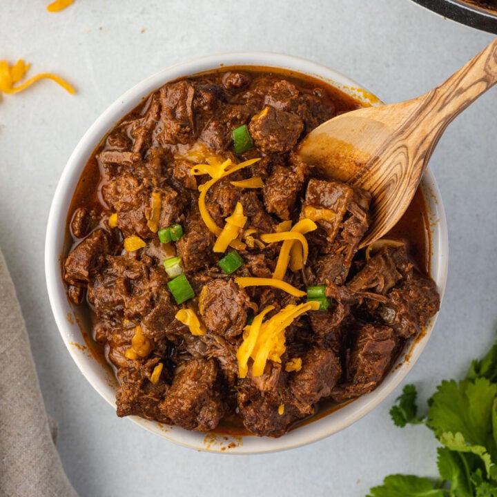 Wooden spoon sticking into bowl of steak chili.