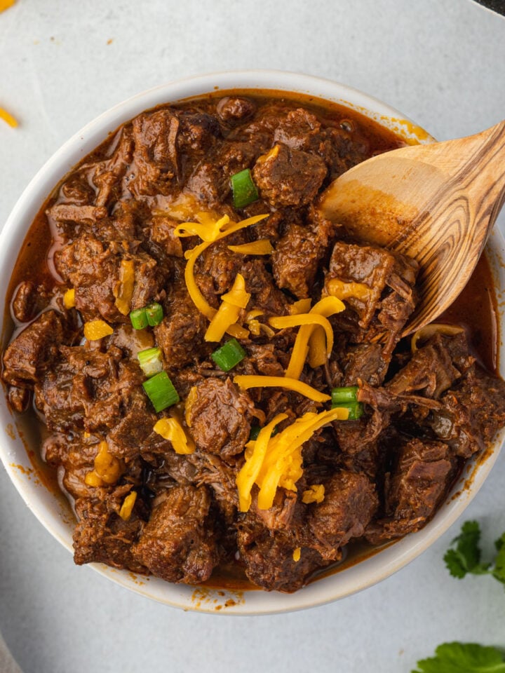 Wooden spoon sticking into bowl of steak chili.